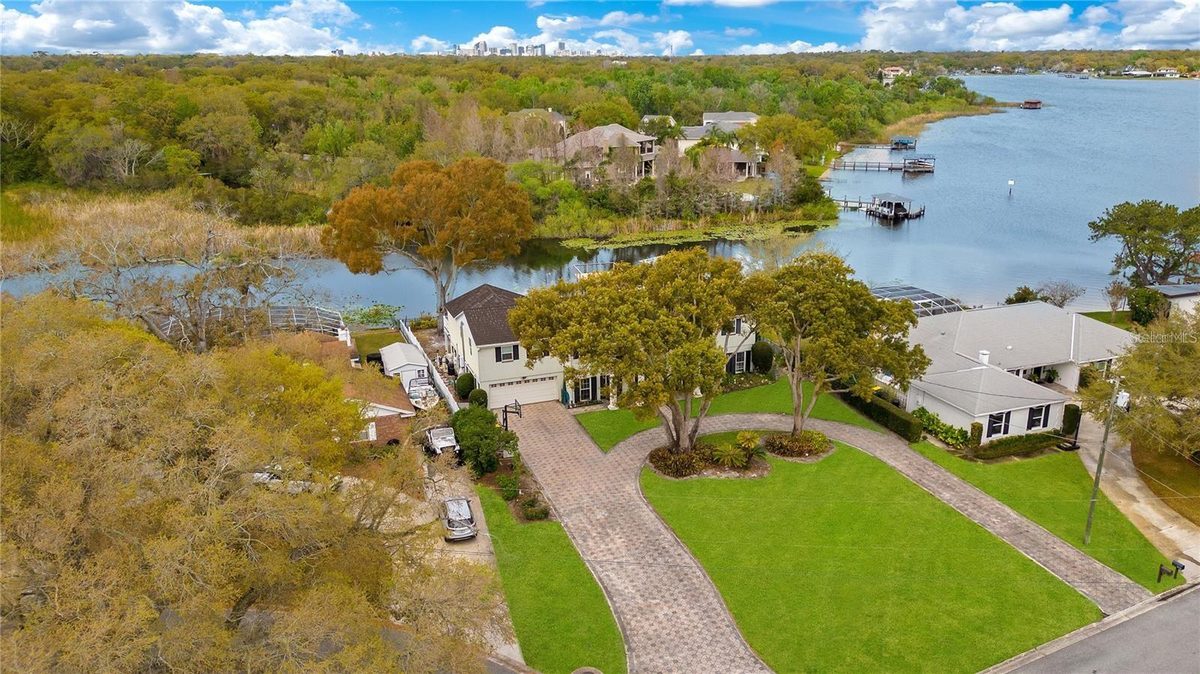 Aerial view of 5018 Saint Denis Court in Belle Isle, a white colonial with a circular drive backing onto Little Lake Conway, with the Orlando skyline in the distance